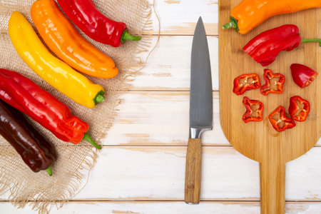 Fresh sweet pepper (bell pepper) on a cutting board with a knife. Chopped pepper pieces are ready to cook. Light wooden table, top view. Space for text.の写真素材