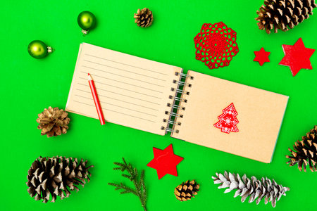 christmas concept. Creative layout made of Christmas green toys, cones, stars and paper notepad with red pencil. flat lay. green background.の写真素材