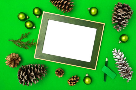 Christmas composition with frame copy space, fir branches, and Christmas baubles on green background. Flat lay, top view festive holiday mockup.の写真素材