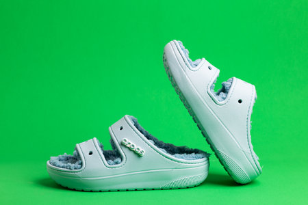 Comfortable, soft Crocs, foam clog shoes with faux fur on green background.のeditorial素材