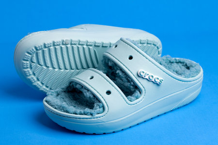 Comfortable, soft Crocs, foam clog shoes with faux fur on blue background.のeditorial素材