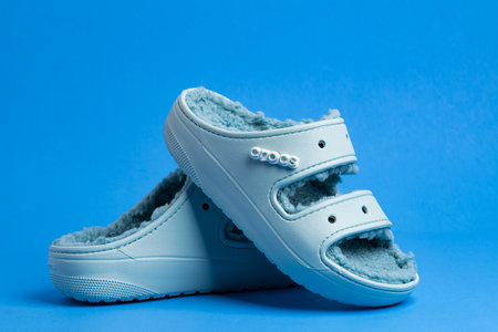 Crocs rubber slippers trimmed with faux fur. Comfortable, light shoes on a blue background.のeditorial素材