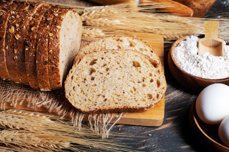 Wheat flour, sliced bread with sesame seeds, wheat ears and straw on an old wooden background