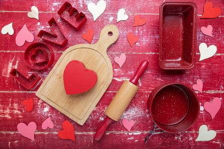 Word LOVE. rolling pins, cookie cutters, and flour on a red wooden background. Heart and cutting board. view from above. Space for text.の写真素材