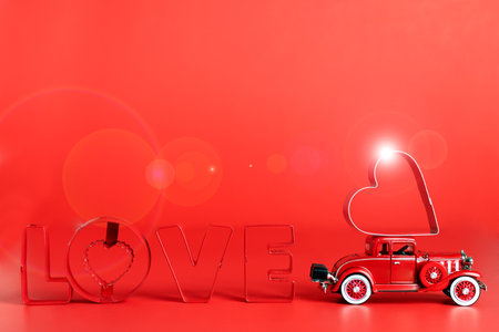 red retro car delivers a red heart on a red background. The word LOVE is written in red letters. The concept of the holiday Valentine's Day and Women's Day. Space for text.の写真素材