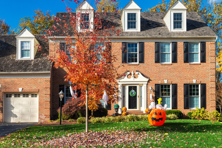 Large Suburban Brick House with Garage and Fall Holiday Decorations. Trimmed lawn and autumn leaves on green grass.のeditorial素材
