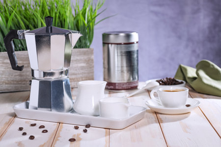 stainless steel geyser coffee maker, a cup of coffee and cream against a gray wall and green decorative grass.の写真素材