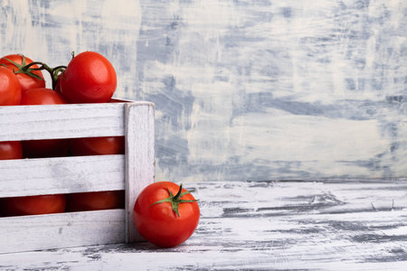 Fresh tomatoes in wooden box on white table. Space for text.の写真素材