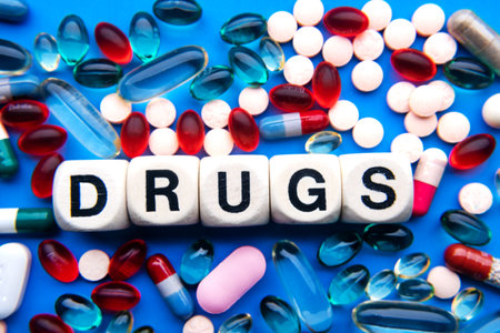 inscription DRUGS in wooden cubes on a blue background of different pillsの写真素材