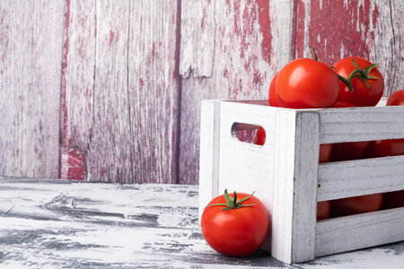 Ripe tomatoes in wooden box on white table. Space for text.の写真素材