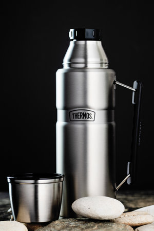 Steel Thermos flask by Termos on a wooden table against a black wall.のeditorial素材