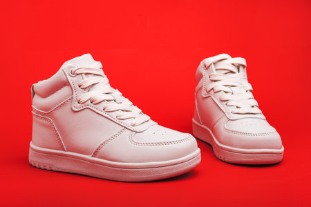 pair of white youth sneakers on red background close-up.の写真素材