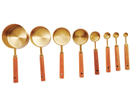 Copper measuring cups/spoons with a wooden handle in sets of different sizes on a white background.の写真素材