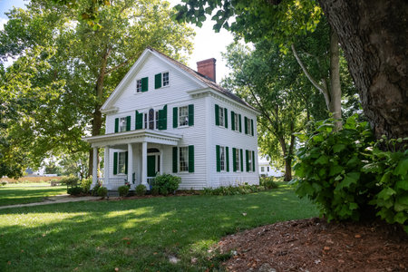 Two-story house in a traditional American style covered with siding. Tree and trimmed lawn in the...