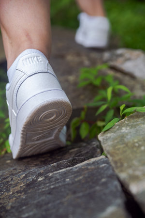 Nike sneakers on the feet of a tourist climbing stones. Close-up. Selective focus, back view.のeditorial素材