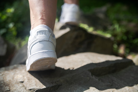Nike sneakers on the feet of a tourist climbing stones. Close-up. Selective focus, back view.のeditorial素材