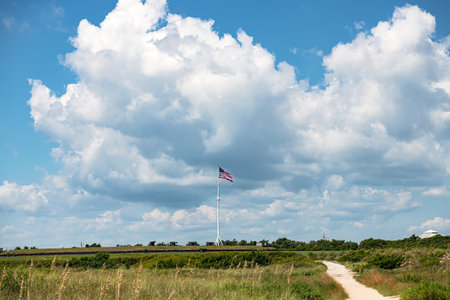 mast with the flag of the United States of America on a hill against a background of clouds and blue...
