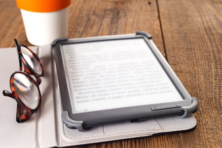 e-book, glasses and cup of coffee on a wooden table. Space for text.の写真素材