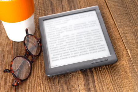 e-book reader and glasses on a wooden table.の写真素材