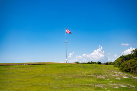 mast with the flag of the United States of America on a hill against a blue sky.の写真素材