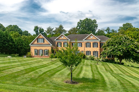 Large, two-story, brick country house with trees and an expansive lawn in the front yard.の写真素材
