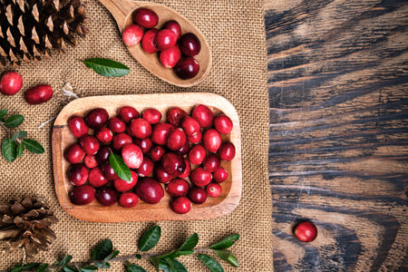 Fresh cranberries in a wooden bowl with spoon on dark wooden table. View from above.Space for text.