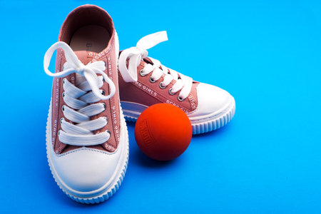 Sports children's sneakers with a ball on a blue background. Space for text.のeditorial素材