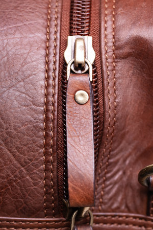 Close-up of a zipper on a brown leather bag. Textured leather, space for text.