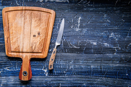 empty wooden cutting board and knife on dark blue table. Preparation of appliances and ingredients for home cooking. Space for text.の写真素材
