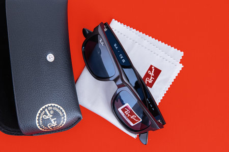 Ray Ban sunglasses case with the company brand logo and Black Ray-Ban sunglasses with plastic frames on a red background.のeditorial素材