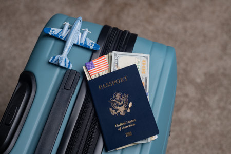 A US citizen passport and American dollars lie next to a model airplane on a travel baggage.