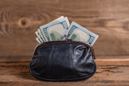 old black genuine leather wallet with banknotes inside on wooden background.の写真素材