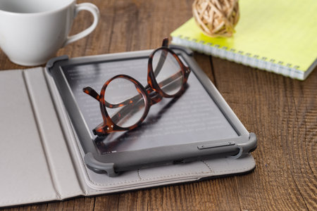 E-book and paper books on the table with a cup of coffee, a laptop and reading glasses. Concepts of...