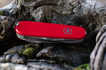 View of closed red Victorinox classical swiss pocket foldable knife in the forest. Close-up.のeditorial素材