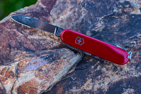 red Victorinox classic pocket folding Swiss Army knife with an open knife blade rests on a stone.のeditorial素材