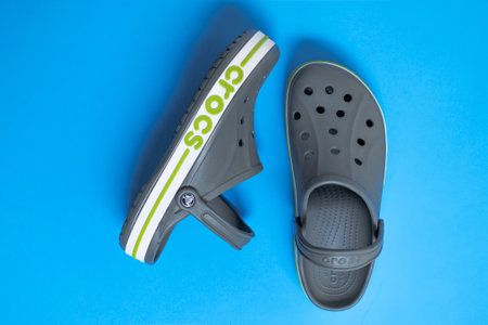 Popular comfortable summer flip-flops with Crocs lettering on blue background. Top view,