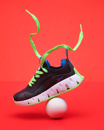 Black sports sneakers reebok with bright green sole and ball on red background.のeditorial素材