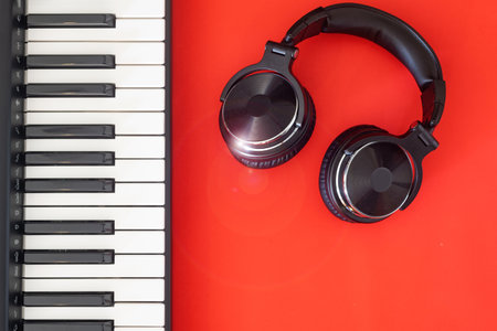 High resolution black and white headphones on keyboard of digital piano. Red background. Place for text.の写真素材