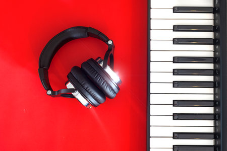 Black and white headphones and black and white keys of digital piano. Red background. Place for text.の写真素材