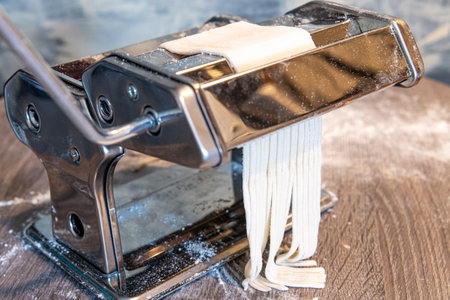 Hand-Cranked Pasta Roller Pressing Fresh Dough into Spaghetti Strandsの写真素材