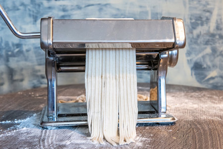 Flour-Dusted Manual Pasta Maker with Raw Dough in Rustic Kitchen Settingの写真素材