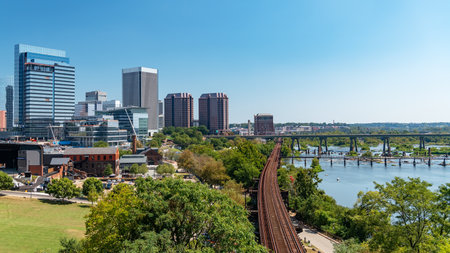 Panoramic view of the Richmond, Virginia skyline featuring modern high-rise buildings, the James River, and historic railroad tracks on a clear, sunny day.の写真素材