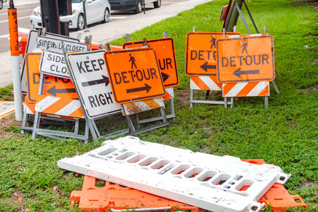 Keep right and detour signs piled up near a street with blurred background cars.