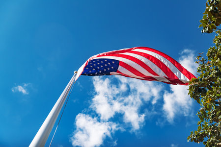 American flag waving against bright blue sky and white cloudsの写真素材