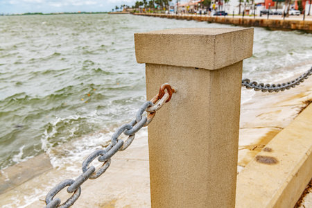 Weathered metal chain on concrete seawall near ocean wavesの写真素材
