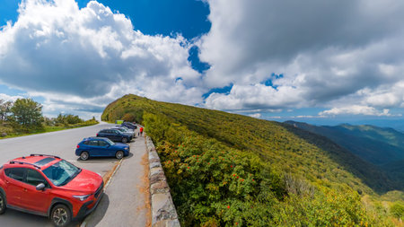 Autumn mountain scenery with a quiet road and parking area, rolling hills, and a clear daytime sky.