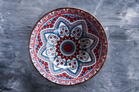Colorful floral ceramic bowl forms a centered mandala pattern on gray stone.