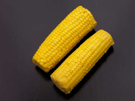 Two sweet-corns on the cob side by side with a black background.の写真素材