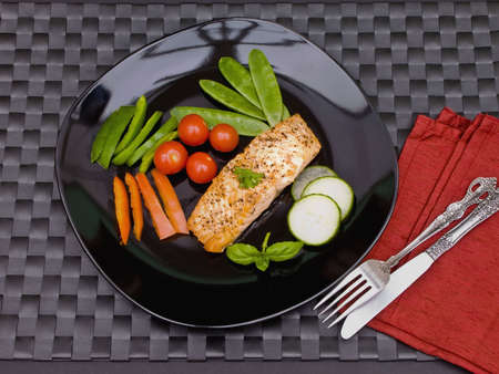 Salmon on black plate with cutlery の写真素材