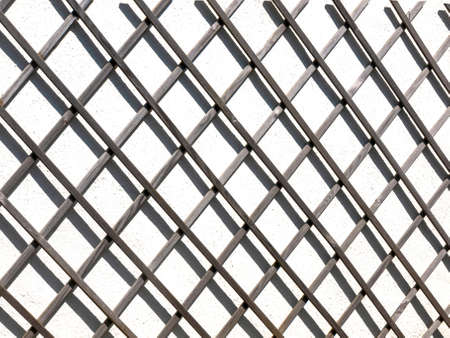 A fence against a white wall casting a shadow. The shadow is casting an abstract pattern against the...